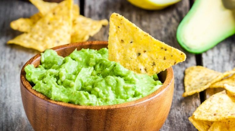 Guacamole in wooden bowl with corn chips dipped in.