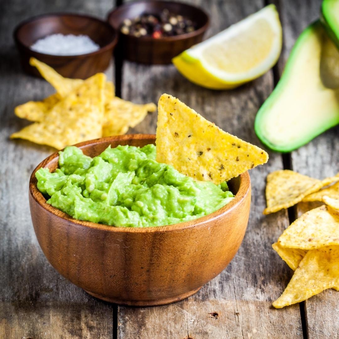 Guacamole in wooden bowl with corn chips dipped in.