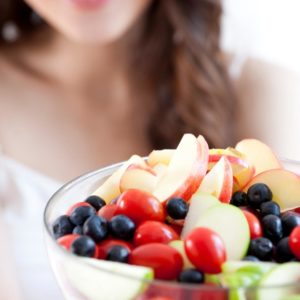 Woman holding bowl with fruit inside.